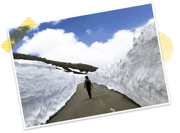 両側に高さ数メートルの雪の壁がある道路を一人の人が歩いています。