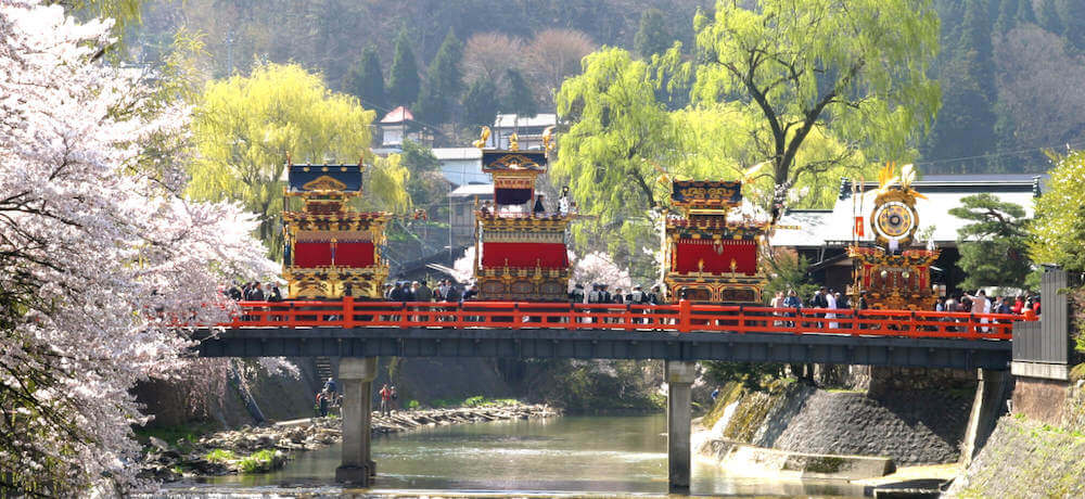 飛騨高山のユネスコ無形文化遺産　春の高山祭（山王祭）です。桜が咲いた中で、橋の上に「山王祭」の屋台組の宝である屋台が並んでいます。